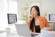 © MINAE - Young asian businesswoman holding pen and thinking while working with laptop and reading financial document in office, business strategy and analysis concept