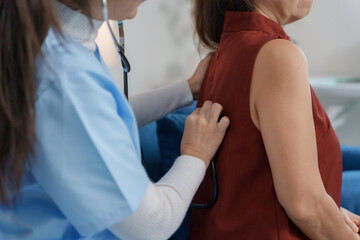 Female doctor using stethoscope examining lungs of senior patient during medical exam