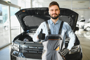 Leinwandbilder - Happy car mechanic showing thumb up near repaired car in car repair shop