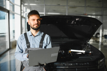 Leinwandbilder - Friendly mechanic in modern car repair shop with car. Professional technician checking vehicle diagnostics and maintenance. Concept of automotive industry and customer service