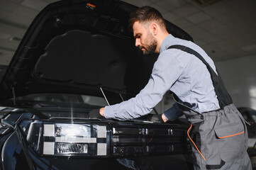 Fototapete - Mechanic Uses a Computer with an Augmented Reality Diagnostics Software. Specialist Inspecting Car's Engine to Quickly Spot Broken Components. Premium Car Service