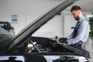 Leinwandbilder - Friendly mechanic in modern car repair shop with car. Professional technician checking vehicle diagnostics and maintenance. Concept of automotive industry and customer service