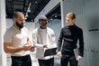 © Parilov - Multiracial team discussing project details in modern office hallway. group comprises african and caucasian males casually dressed, engaging in conversation, sharing ideas, and using digital tablets.