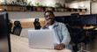 © Parilov - African american man smiling confidently while sitting at desk with laptop in contemporary office setting. indoor plants and organized bookshelves create stylish and productive atmosphere.