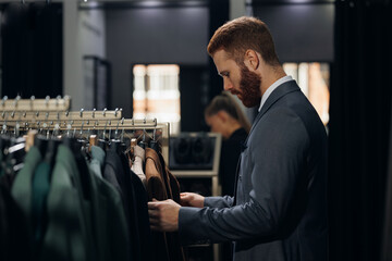 Wall Mural - Portrait handsome client man in menswear store chooses suit. Luxury designer atelier shop