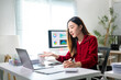 © Apichat - A woman in a red shirt is sitting at a desk with a laptop and a keyboard