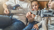 © Mariia - Father playing guitar for daughters sitting on floor next to bed.
