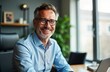 © Maryna - Smiling middle-aged businessman sits at office desk, working on laptop. Wears glasses, light blue shirt. Looks happy, focused. Image taken in office environment with modern feel. Background includes