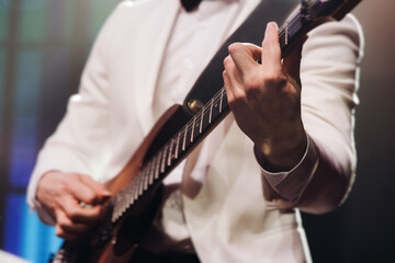 Concert view of an electric guitar player with vocalist and rock band performing in a club, male musician guitarist on stage with audience in a crowded concert club hall arena, hands on a guitar