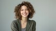 © sergiokat - An elegant woman with curly, beautiful hair, smiling warmly, dressed in an edgy and fashionable outfit, standing against a clean gray background.