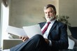 © opolja - Mature businessman checking and reading documents while working on business project and sitting couch in modern office