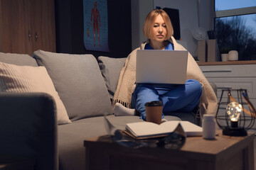 Sticker - Female nurse with plaid using laptop on sofa at hospital in evening