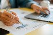 © Satori Studio - Close-up of hands working on financial charts and laptop, illustrating business analysis and productivity.