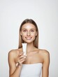 © Danudet.C - Smiling woman holding skincare cream tube against a neutral background, showcasing beauty, confidence, and self-care routine with a radiant smile
