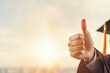 © UnderTheSun - Person giving a thumbs-up gesture in a graduation cap, symbolizing achievement and celebration against a soft, glowing background.