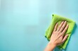 © Maryna - Young woman cleans surface with green rag. Top view closeup on hand wiping table wall floor in kitchen bathroom room. Light pastel blue background. Empty space for logo text. Cleaning concept. Home