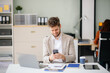 © laddawan - Confident businessman working on finance analysis with a tablet and laptop at office desk.