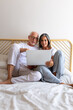 © Daniel - Front view vertical portrait of mature couple using laptop together relaxing sitting on the bed.
