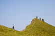 © yaqui_villegas - A woman walks alone on a lush green hill, enjoying the serene landscape and the bright blue sky above, embodying a peaceful connection with nature and solitude.