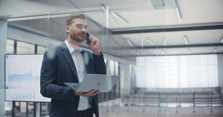 Poster - Young Entrepreneur Negotiating a Deal on Phone while Checking Emails on Laptop Computer. Confident and Professional Man Communicates with Clients while Standing in Office, Looking Out of the Window