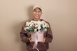 © New Africa - Smiling delivery man holding gift box with beautiful floral composition on beige background