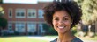 © Kultivad - Smiling Black female student with afro hairstyle outdoors on sunlit school campus showcasing happiness and youthfulness with greenery and academic buildings in background