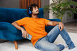 © ViDi Studio - Young man wearing casual clothes sits near blue sofa couch use mobile cell phone listen music in headphones stay home hotel flat rest relax spend free spare time in living room indoor. Lounge concept.