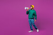 © ViDi Studio - Full body young happy Indian man he wear green hoody yellow hat casual clothes hold in hand megaphone scream announces discounts sale Hurry up isolated on plain purple background. Lifestyle concept.