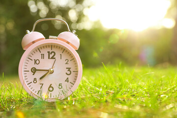 Wall Mural - Pink alarm clock on green grass outdoors. Space for text