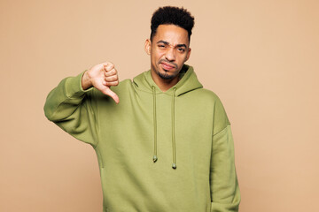 Wall Mural - Young sad upset man of African American ethnicity wear green hoodie casual clothes showing thumb down dislike gesture isolated on plain pastel light beige background studio portrait Lifestyle concept