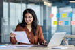 © Liubomir - Paperwork office work, young successful latina woman working with documents and contracts inside office at workplace. Satisfied woman smiling checking, reports and tax forms.