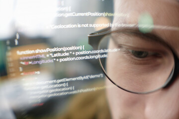 extreme close up of male it programmer wearing glasses looking at computer screen with lines of code