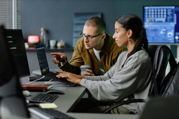 side view of male it programmer pointing at laptop screen helping female colleague with code debuggi