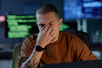 portrait shot of male programmer exhausted from work overload sitting at desk with eyes closed after