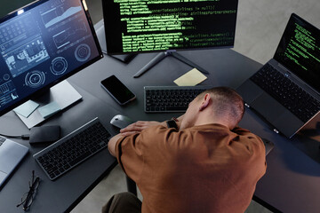 top view of exhausted male programmer lying on desktop with several computers resting from work over