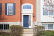 © Joseph Hendrickson - The front door of a red brick home with steps leading up to white trim around a window and blue front door.