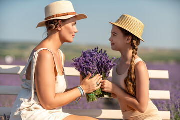 Wall Mural - A woman and a child are sitting on a bench in a field of purple flowers lavande. The woman is holding a bouquet of flowers and the child is holding a bouquet of flowers as well