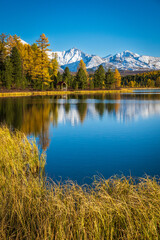 Wall Mural - Serene view of a reflective lake with golden trees and snow-capped peaks in background