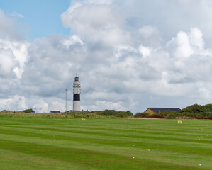 White lighthouse with a black stripe behind a meadow, Sylt, Germany