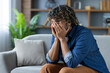 © Liubomir - Desperate and depressed man sitting on sofa in living room at home, burying face in hands, feeling sad and disappointed.