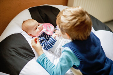 Happy little kid boy with newborn baby girl, cute sister. Siblings. Brother and baby playing with colorful toys and rattles together. Kids bonding. Family of two bonding, love