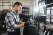 © Serhii - Portrait man mechanic holding new tyre on background store, car tire service concept