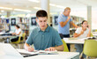 © JackF - Positive young man in casual clothes working remotely using a computer in a quiet library