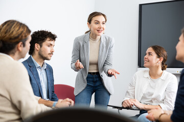 Wall Mural - Professional business coach woman standing near interactive board and conducting training different people gathered in circle in auditorium