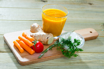 Glass of fresh carrot juice with grated ginger on wooden board