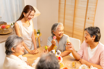 Happy Asian elderly woman meeting party afternoon tea at home. Adult daughter serving bakery and tea to elderly mother and friends on the table. Retired people mental healthcare and wellness concept.