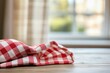 © BerkahStock - Red and white checkered tablecloth on wooden table near window.