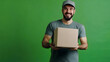 © Erika - hombre joven empleado repartidor de paquetes en empresa de paqueteria a domicilio un fondo verde con un hombre joven sosteniendo una caja de carton un paquete con espacio de copia