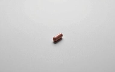 A single  capsule pill resting on a clean white surface, casting a subtle shadow.