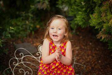 Wall Mural - Portrait of female child wearing bright red dress sitting in natural garden setting